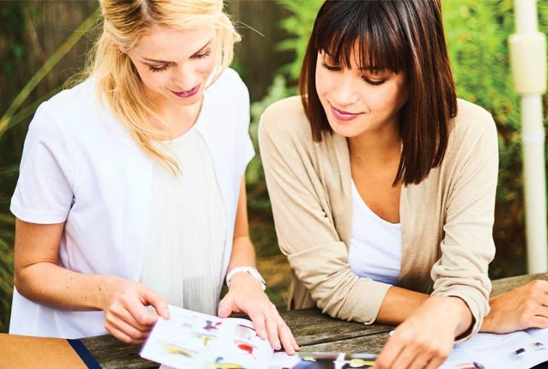Bild mit zwei jungen Damen, welche sich die Tupperware-Monatsangebote, Flyer und Kataloge ansehen